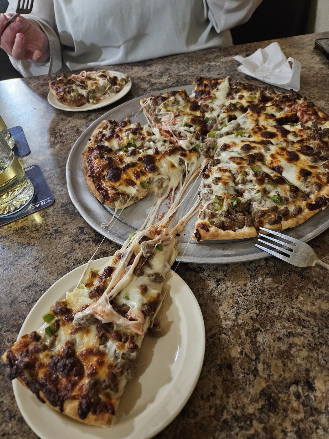 A slice of Pizza Glen pizza lifting off the pan, cheese stretching behind it