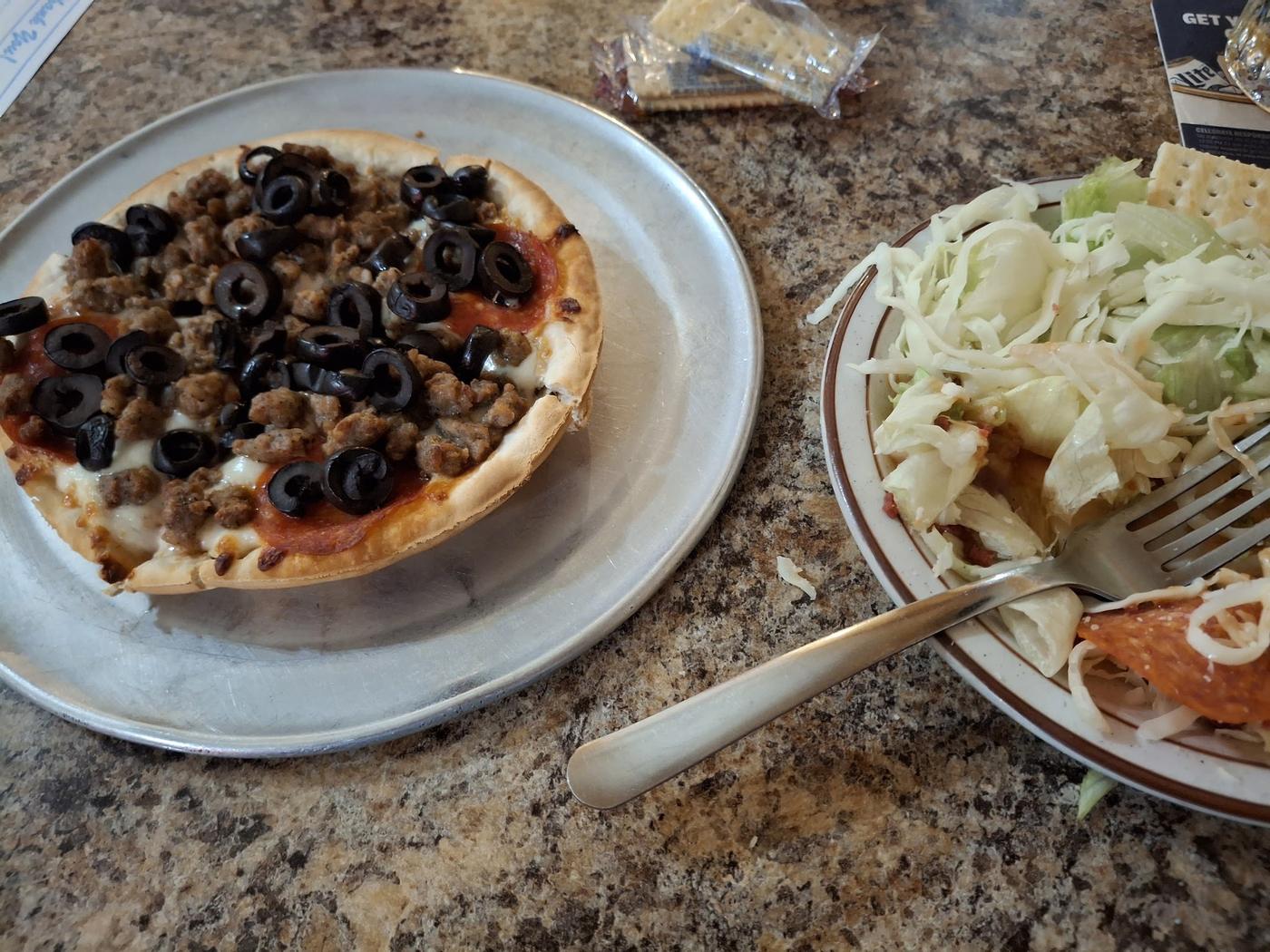 A small round pizza on a metal pan beside a house salad