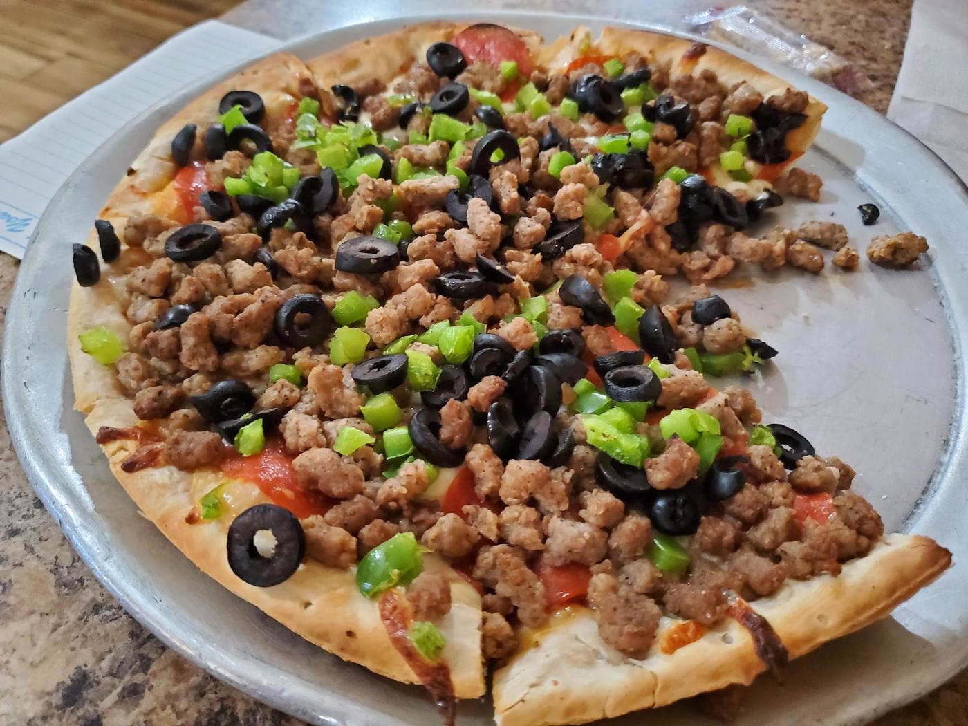 A round pizza topped with sausage, green pepper and black olive